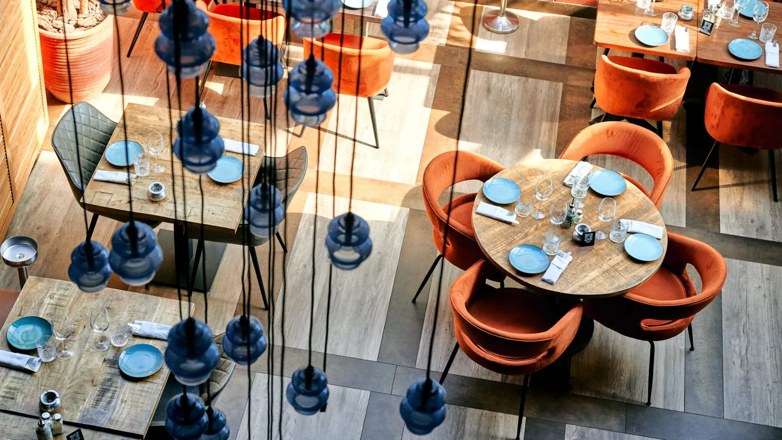 Vue plongeante sur les tables, fauteuils orange et suspensions en verre bleu